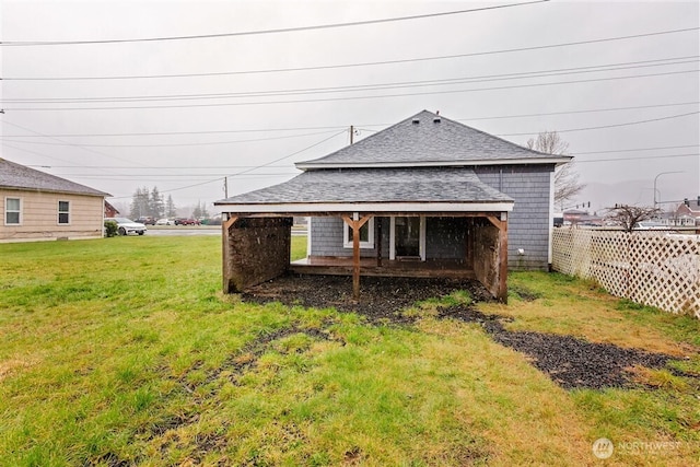 back of house with roof with shingles, a lawn, and fence