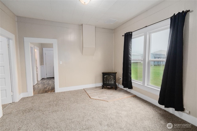 carpeted empty room featuring a wood stove and baseboards