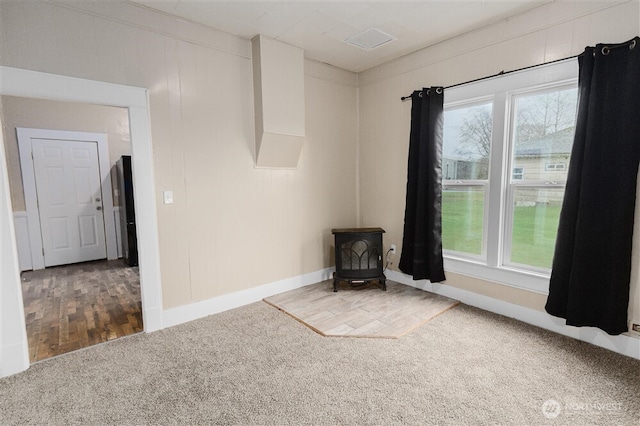 carpeted empty room with a wood stove, plenty of natural light, and baseboards