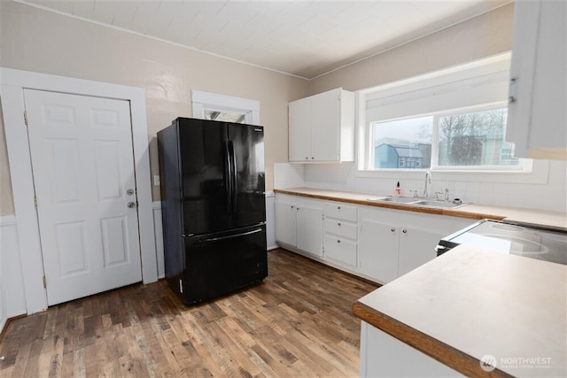 kitchen with light countertops, a sink, freestanding refrigerator, and white cabinets