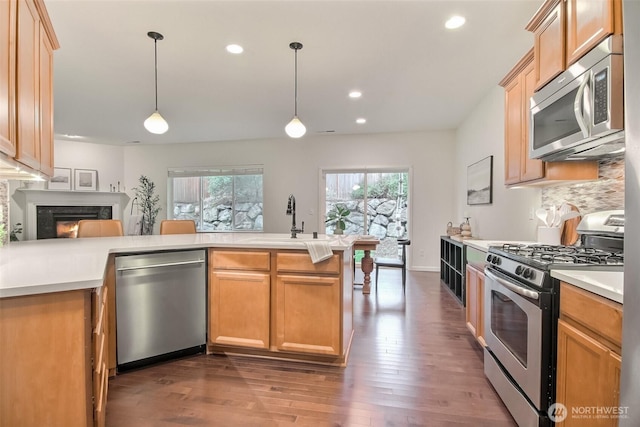 kitchen featuring appliances with stainless steel finishes, light countertops, a sink, and decorative light fixtures