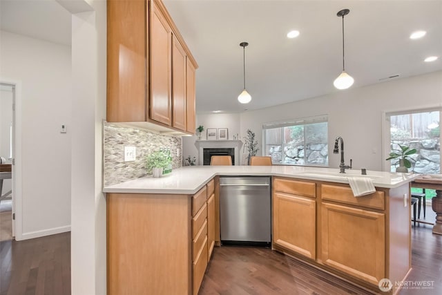 kitchen featuring light countertops, hanging light fixtures, a sink, dishwasher, and a peninsula