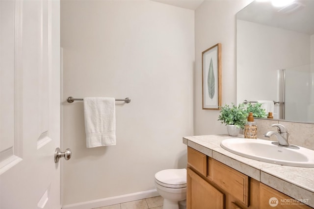 bathroom featuring toilet, a shower with shower door, vanity, baseboards, and tile patterned floors