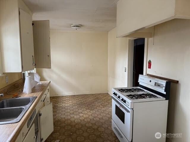 kitchen with gas range gas stove, dark floors, light countertops, white cabinetry, and a sink