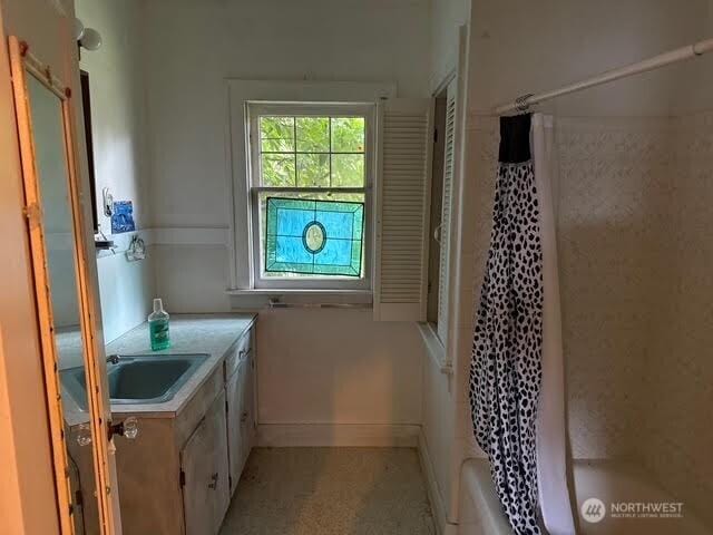 bathroom featuring vanity, shower / tub combo, and baseboards