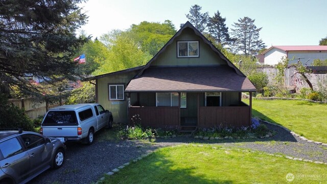 view of front facade featuring covered porch, roof with shingles, a front yard, and fence