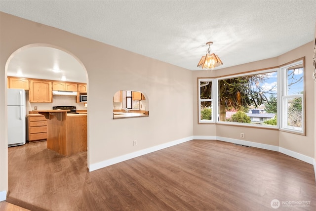 unfurnished dining area featuring light wood-style flooring, visible vents, arched walkways, and baseboards