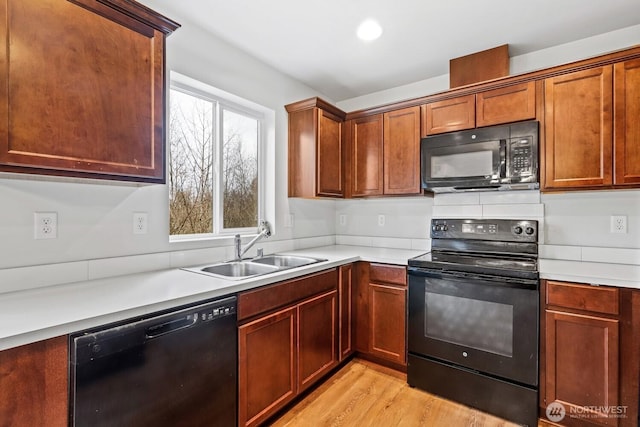 kitchen featuring light wood-style flooring, a sink, light countertops, black appliances, and brown cabinetry