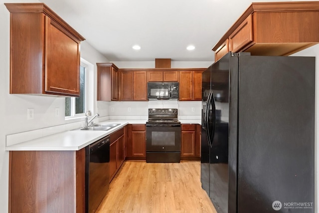 kitchen with black appliances, brown cabinetry, a sink, and light countertops