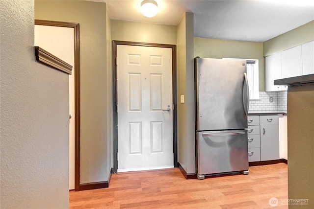 kitchen with light wood-style flooring, white cabinets, backsplash, freestanding refrigerator, and dark countertops