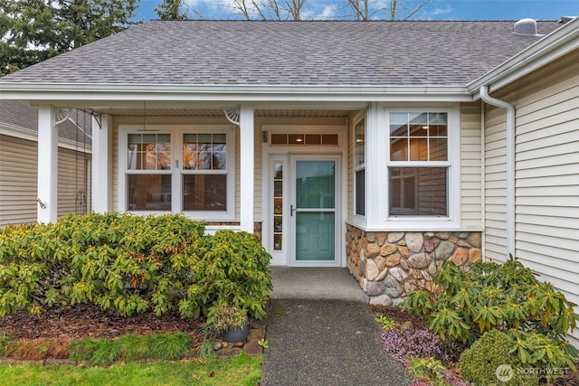 view of exterior entry featuring stone siding and roof with shingles