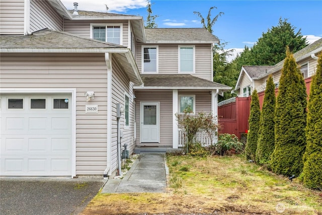 view of front of property with a shingled roof, an attached garage, and fence