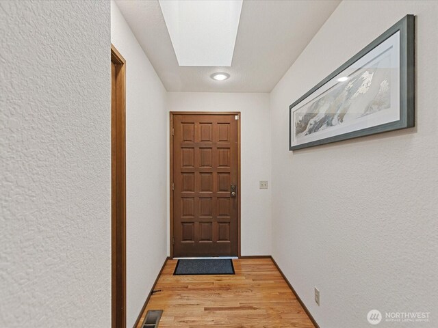 entryway featuring a skylight, baseboards, visible vents, a textured wall, and light wood-type flooring