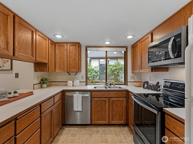 kitchen with light countertops, appliances with stainless steel finishes, brown cabinetry, and a sink