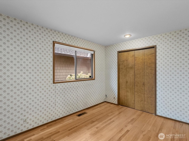 unfurnished bedroom with a closet, visible vents, wood finished floors, baseboards, and wallpapered walls