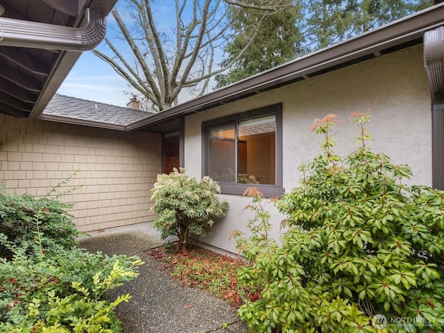 doorway to property featuring roof with shingles and stucco siding