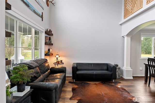 living room with baseboards, arched walkways, a towering ceiling, dark wood-style flooring, and ornate columns