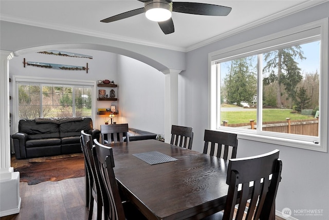 dining area featuring arched walkways, decorative columns, ornamental molding, a ceiling fan, and wood finished floors