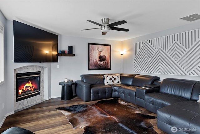 living room with baseboards, visible vents, a ceiling fan, a tiled fireplace, and dark wood-style floors