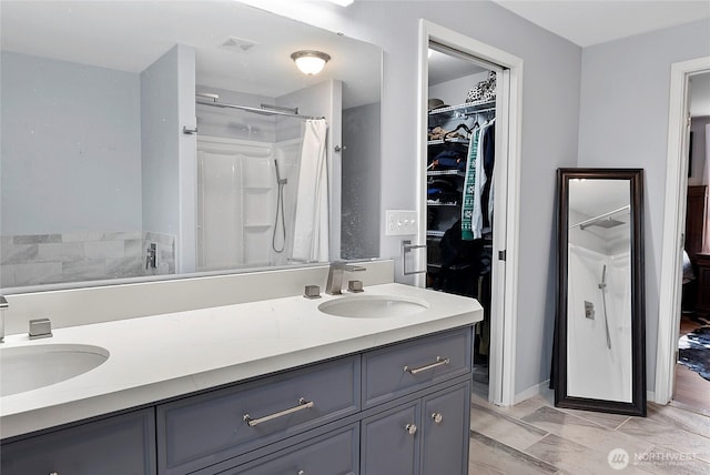 bathroom featuring a walk in closet, visible vents, a sink, and double vanity