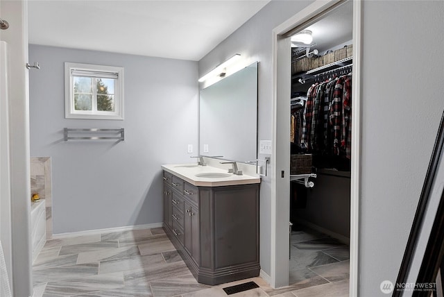 full bathroom with double vanity, a spacious closet, a sink, and a bath