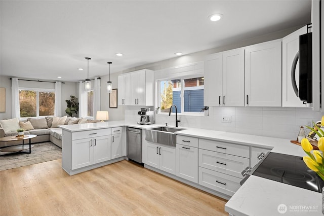 kitchen featuring open floor plan, stainless steel appliances, white cabinetry, pendant lighting, and a sink