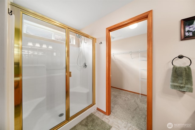 full bath featuring a walk in closet, a shower stall, and baseboards