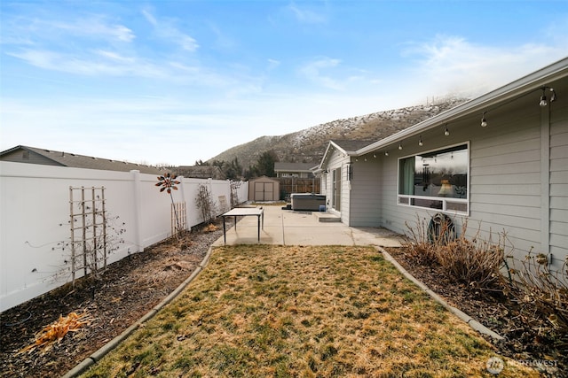 view of yard with a hot tub, a patio, a fenced backyard, a storage unit, and a mountain view