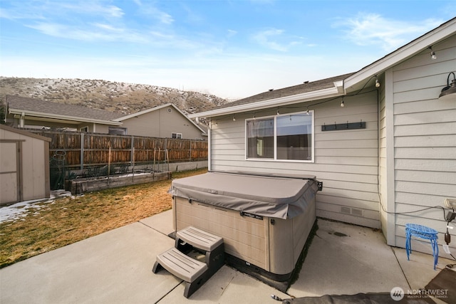 view of patio featuring an outbuilding, a storage unit, fence, and a hot tub