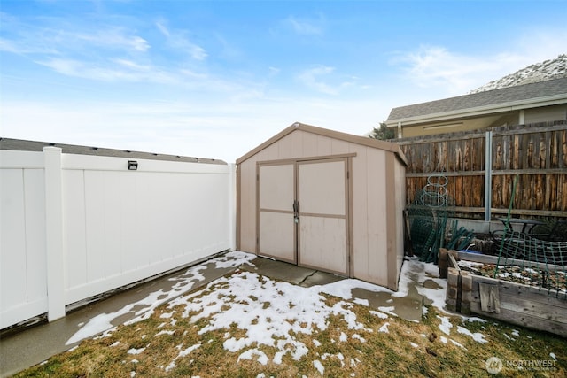 snow covered structure featuring a storage shed, a fenced backyard, a vegetable garden, and an outbuilding