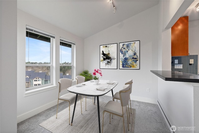 dining space with lofted ceiling, light carpet, rail lighting, and baseboards