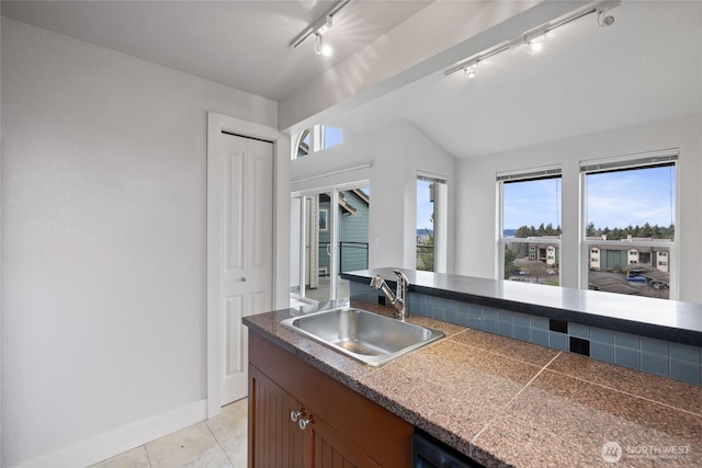 kitchen with light tile patterned floors, a sink, baseboards, vaulted ceiling, and brown cabinets