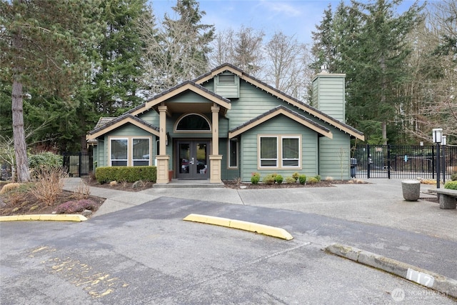 view of front of house with uncovered parking, french doors, fence, and a chimney