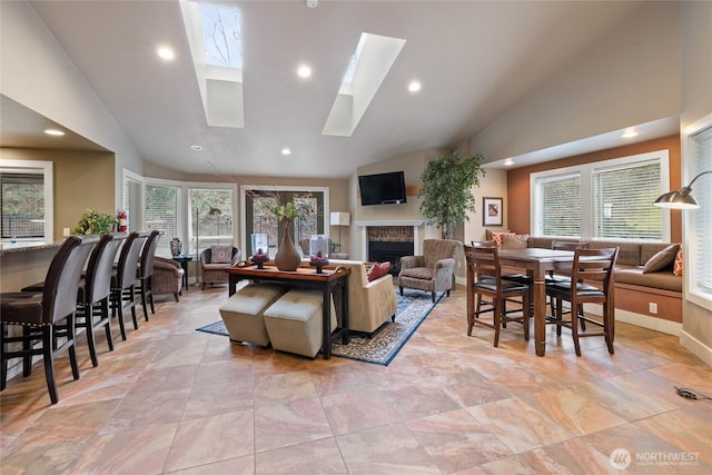 living area featuring high vaulted ceiling, a skylight, a fireplace, and a healthy amount of sunlight