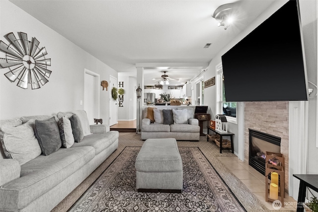 living room featuring light tile patterned floors, visible vents, a tile fireplace, and a ceiling fan