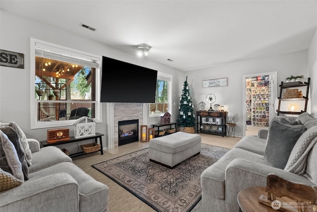 carpeted living room with visible vents and a stone fireplace