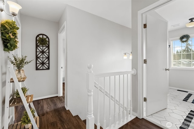 corridor with visible vents, wood finished floors, an upstairs landing, and baseboards