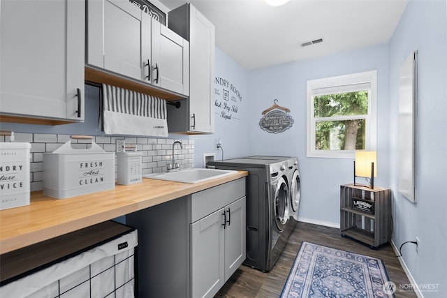 clothes washing area with cabinet space, visible vents, dark wood finished floors, separate washer and dryer, and a sink