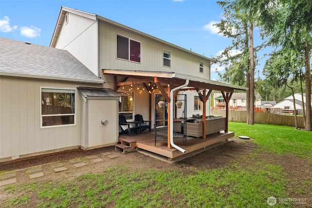 rear view of property featuring roof with shingles, fence, a deck, and a yard