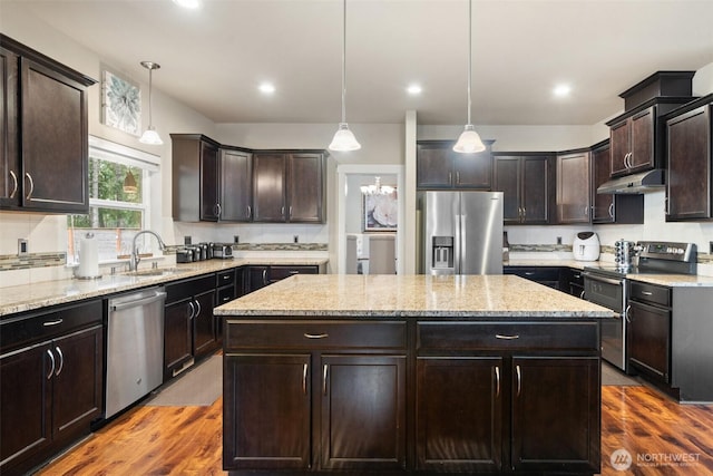 kitchen with dark brown cabinetry, under cabinet range hood, a sink, a kitchen island, and appliances with stainless steel finishes