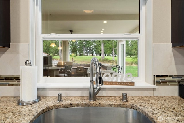 kitchen featuring tasteful backsplash, light stone counters, and a sink