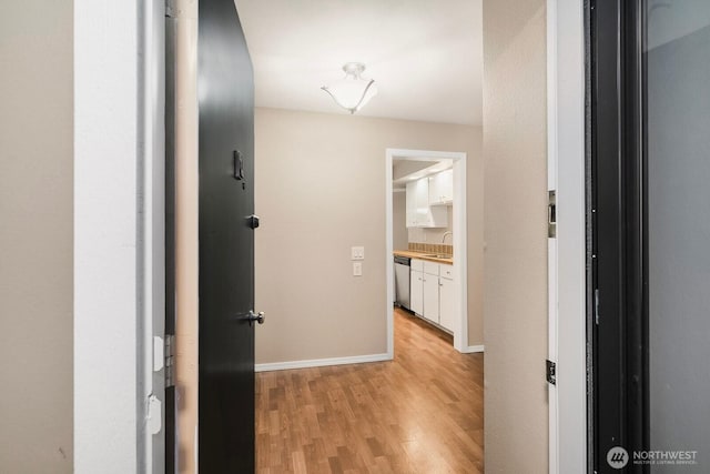 hall with light wood-style floors, a sink, and baseboards