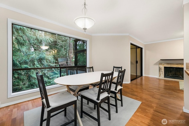 dining space with baseboards, a fireplace, wood finished floors, and crown molding