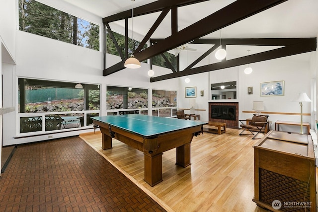 game room with high vaulted ceiling, brick floor, a fireplace, a ceiling fan, and beam ceiling