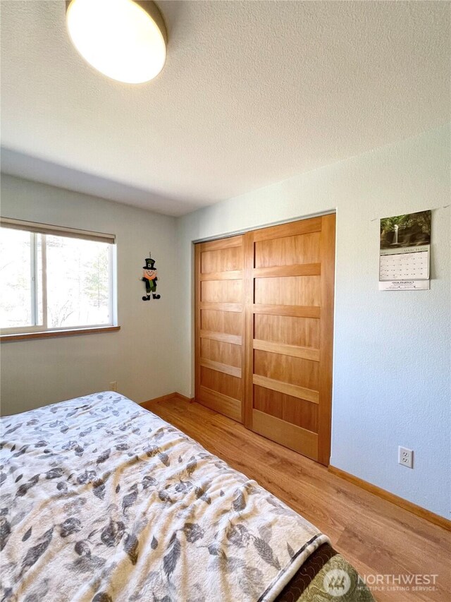 bedroom with a textured ceiling, wood finished floors, and baseboards