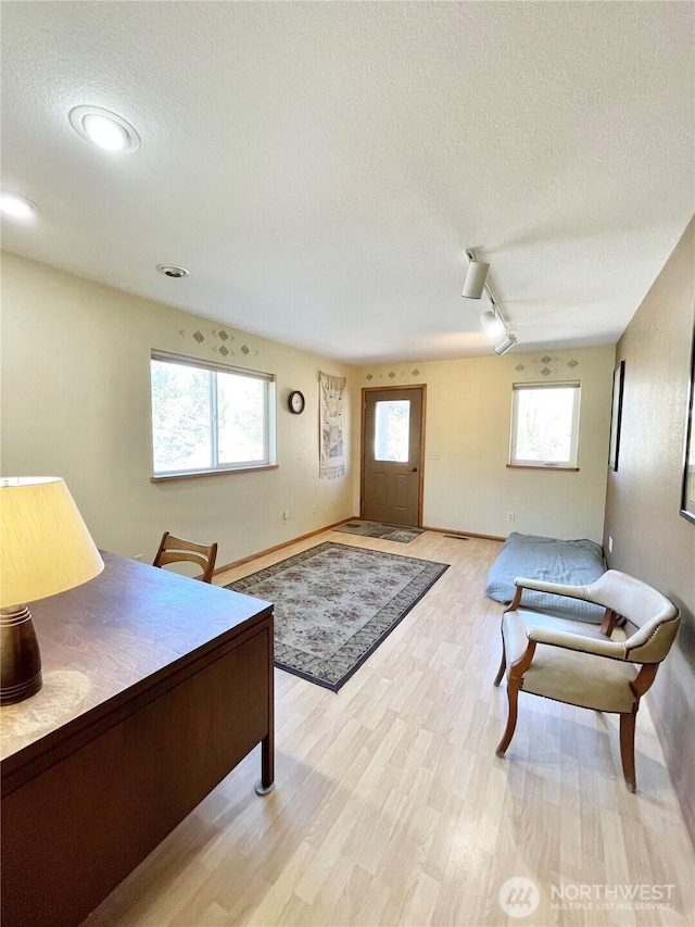 interior space featuring light wood-style flooring, track lighting, a textured ceiling, and baseboards