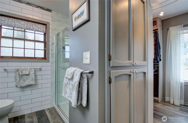 bathroom with toilet, a stall shower, wood finished floors, and a wealth of natural light