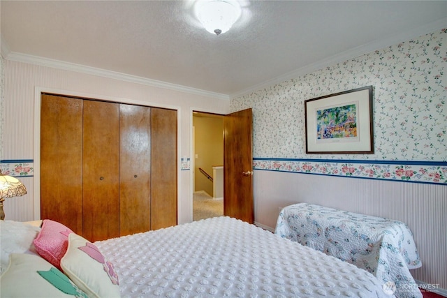 carpeted bedroom featuring a textured ceiling, ornamental molding, a closet, wainscoting, and wallpapered walls