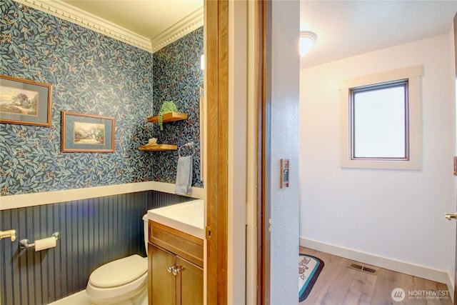 bathroom with a wainscoted wall, visible vents, toilet, wood finished floors, and wallpapered walls