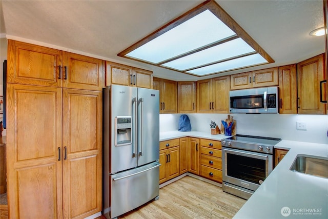 kitchen with stainless steel appliances, brown cabinets, light countertops, and light wood-style floors